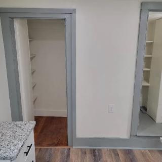 A room with a closet and a large mirror, featuring gray trim and hardwood flooring.