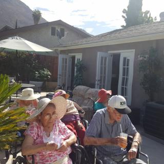 A group of seniors enjoying a sunny day on a patio, seated in wheelchairs and wearing hats.