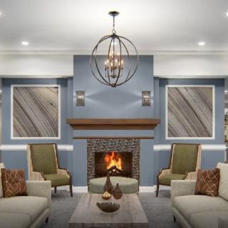 A stylishly decorated living room featuring a central fireplace with surrounding armchairs and sofas, complemented by modern art and a decorative chandelier.