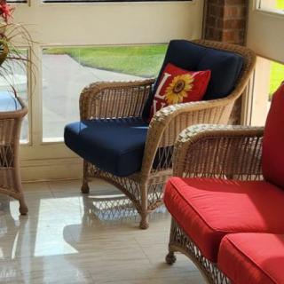A sunlit room featuring wicker chairs with colorful cushions and a decorative pillow.