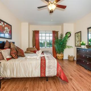 A cozy bedroom with elegant decor, featuring a bed, ceiling fan, artwork, and large window.
