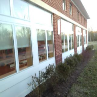 Exterior view of a brick building with large windows and surrounding bushes.