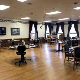An interior room with chairs and tables arranged in a spacious setting, featuring large windows with curtains.
