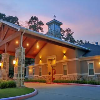 A warmly lit building entrance in the evening with a covered driveway and surrounding trees.