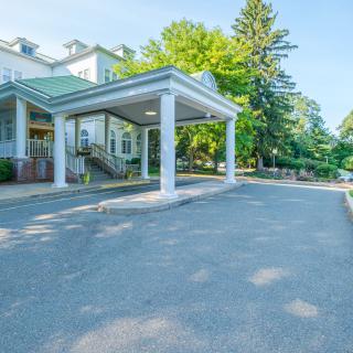 A residential building entrance with a driveway, surrounded by trees.