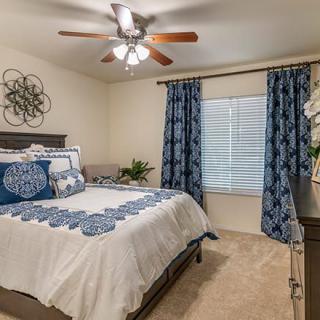 A cozy bedroom with blue and white decor, featuring a bed, curtains, wall art, and a ceiling fan.