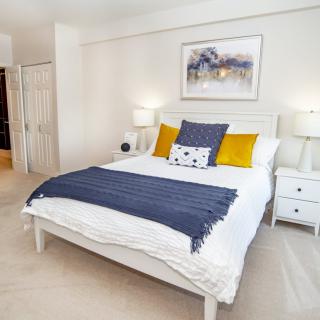 A modern and cozy bedroom featuring a white bed with decorative pillows, flanked by nightstands and lamps, complemented by wall artwork.