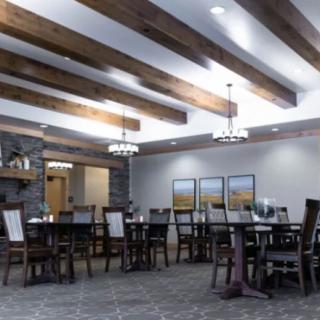 A spacious dining room featuring elegant chandeliers, wooden beams, and neatly arranged tables and chairs.