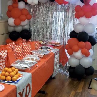 A festive party setup with colorful balloon decorations and a table covered in orange-themed items.