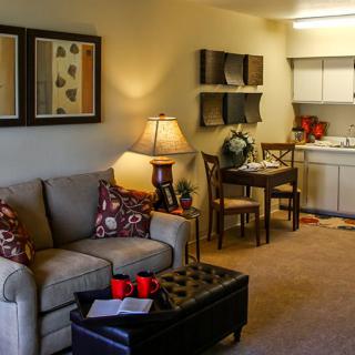 A cozy living room with a sofa, table, and lamp, adjacent to a small kitchen area.