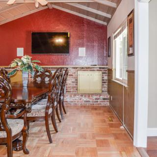 A cozy dining room with a wooden table, elegant chairs, and a brick accent wall featuring a mounted television.