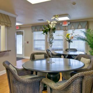 A cozy indoor dining area with a round table and wicker chairs, adorned with plants and natural light.