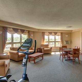 A spacious living room featuring an exercise bike, sofas, and a dining area with large windows allowing natural light.