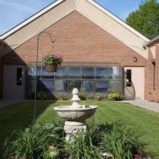A serene garden setting featuring a fountain in front of a brick building.