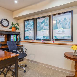 A neatly arranged office space with a desk, chair, framed artwork, and a wall clock.