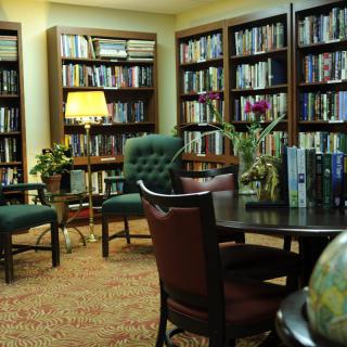 A cozy library reading room with bookshelves, chairs, and a lamp.