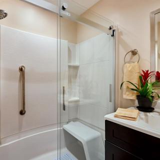 A modern bathroom featuring a glass-enclosed shower, grab bars for safety, and a vanity with decorative indoor plants and towels.