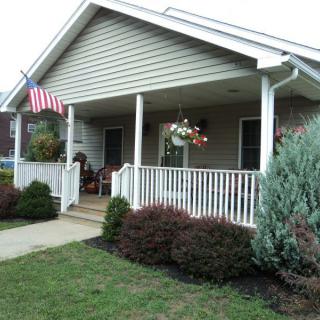 A cozy house with a front porch, decorated with an American flag and surrounded by a well-maintained garden.