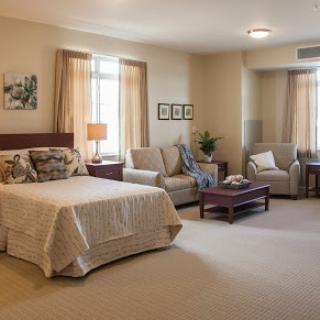 A spacious and inviting bedroom area featuring a comfortable bed, seating, and soft natural lighting.