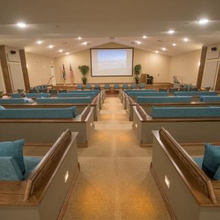 An interior view of a church with rows of pews and a large projection screen at the front.