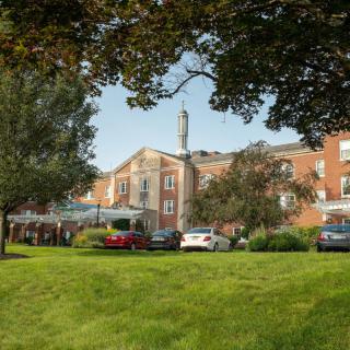 A hotel building surrounded by lush greenery and parked cars on the lawn.