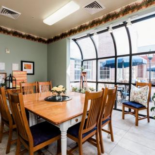A well-lit dining room with wooden furniture and large windows letting in natural light.