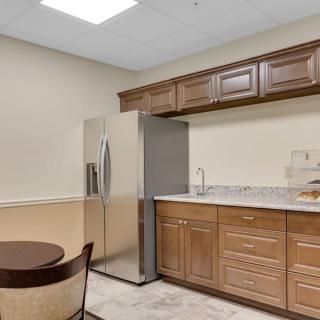 A modern kitchen with wooden cabinets, a stainless steel refrigerator, and a small dining area.