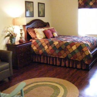A cozy bedroom featuring a colorful quilt on the bed, wooden floors, and a soft area rug.
