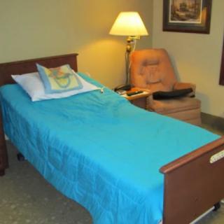 A room with a hospital bed, a lamp, and a chair.