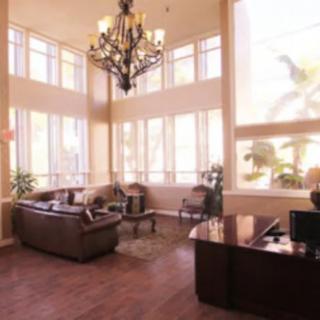A well-lit lobby featuring a large chandelier, tall windows, and elegant furniture including sofas and a desk.