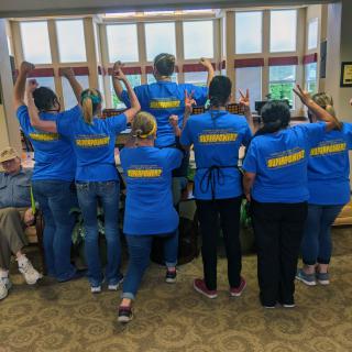 A team wearing matching blue shirts poses cheerfully indoors.