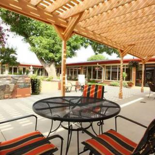 A cozy courtyard patio featuring a pergola, table, and chairs with a scenic garden view.