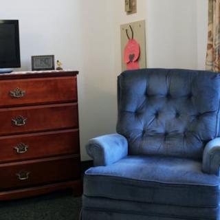 A cozy living room corner with a blue armchair and a wooden dresser next to a small television.