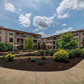 A beautifully landscaped apartment complex with a garden and pathways under a cloudy sky.