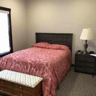 A cozy bedroom with a bed covered in a patterned red comforter, accompanied by a nightstand and lamp.