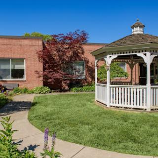 A serene garden featuring a white gazebo, surrounded by lush greenery and a clear blue sky.
