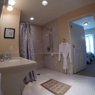 A well-lit bathroom with a shower area, robe, and sink.