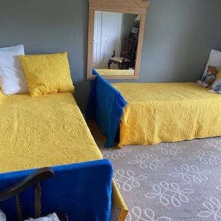 A bright and cozy bedroom featuring twin beds with yellow bedding and blue accents, complemented by a large mirror.