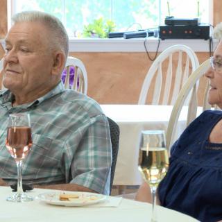 An elderly couple sitting at a dining table with wine glasses.