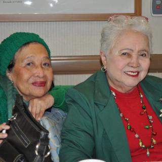 Two women sitting together, smiling and dressed in festive colors.