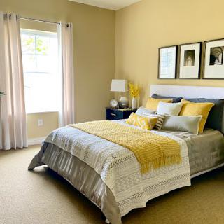 A cozy and inviting bedroom featuring a blend of yellow and gray tones, complemented by soft natural light from the window.