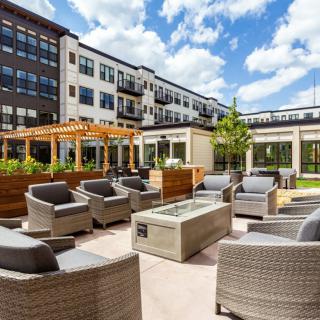 A modern outdoor patio area at an apartment complex with comfortable seating and greenery under a bright sky.
