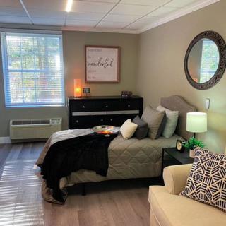 A cozy and well-decorated bedroom featuring a comfortable bed, a mirror on the wall, stylish decor, and soft lighting.