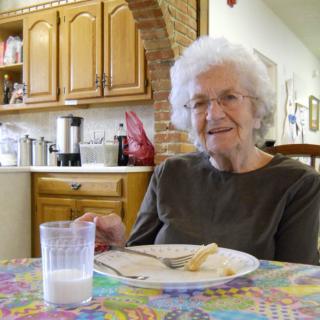 An elderly woman enjoying a meal in her kitchen.
