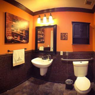 A cozy bathroom with orange walls, featuring a sink, mirror, and toilet.