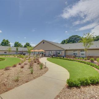 A landscaped garden with a pathway leading to a modern building under a blue sky.