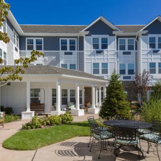 A sunny day view of a residential building with a landscaped garden and outdoor seating area.