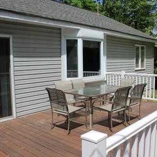 An outdoor deck with a glass patio table and four chairs next to a house.