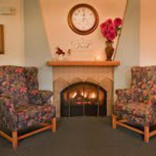 A cozy living room with two floral armchairs flanking a fireplace topped by a clock and vase of flowers.