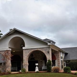 A brick house with arched entryways and a well-maintained front yard under a cloudy sky.